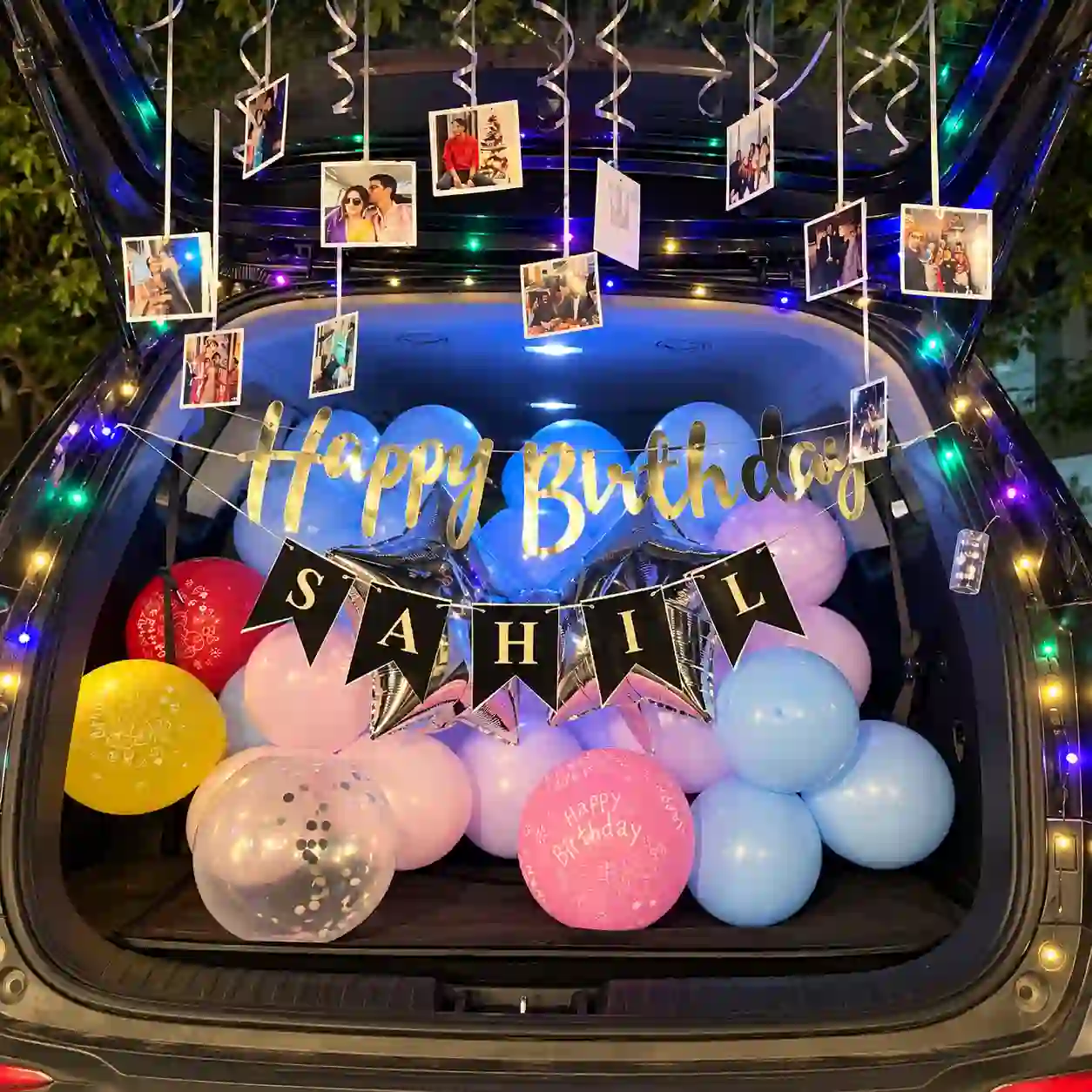 Birthday car boot decoration with blue and pastel balloons, silver star foil balloons, Happy Birthday banner, personalized name bunting, hanging photographs and colorful fairy lights.