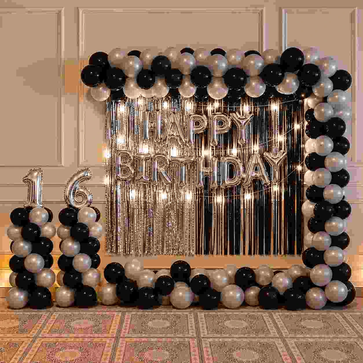 Elegant black and silver 16th birthday decoration with 120-balloon half arch, silver and black fringe curtains, Happy Birthday foil balloons, silver number 16 balloon and floor balloon clusters.