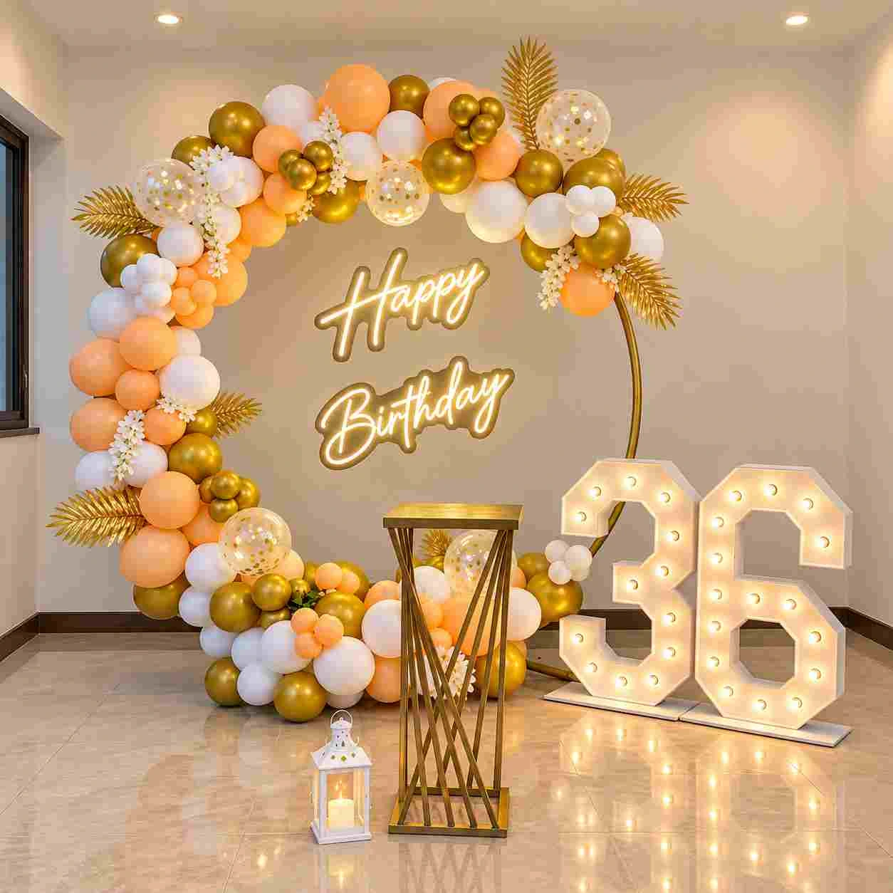 Elegant peach, white and gold 36th birthday decoration with organic balloon arch, Happy Birthday sign, illuminated number 36, floral accents and decorative lantern.